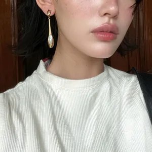 Gros plan de boucles d'oreilles pendantes dorées avec pierre œil-de-chat sur modèle
