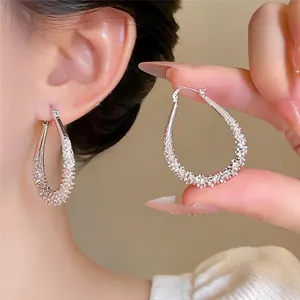 Close-up detail of silver-tone water-drop hoop earrings with a sparkling textured finish.