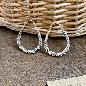 Close-up of silver-toned teardrop hoop earrings with a textured sparkling finish.