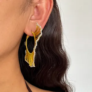 Gros plan détaillé d'une boucle d'oreille géométrique tissée or et argent portée à l'oreille.