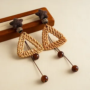 Detailed view of woven rattan triangle earrings with star stud and brown glass bead tassels.