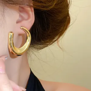 Detailweergave van dikke goudkleurige C-vormige minimalistische oorringen op model.