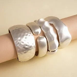 Close-up of silver-toned chunky metal bracelets with hammered and rippled textures.