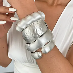 Close-up detail shot of chunky textured silver cuff bracelets layered on a model's arm