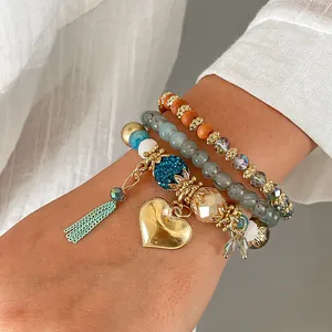 Close-up of bohemian multi-layered beaded bracelet stack with gold heart and tassel charms