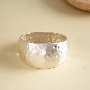 Close-up of a wide silver-finished bangle featuring a unique hammered and wrinkled metal texture