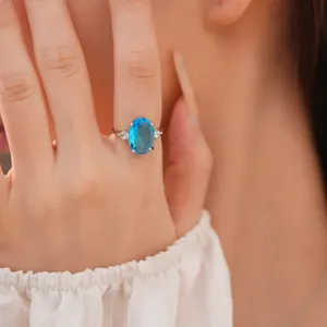 Detailed close-up of an elegant oval blue zircon ring with side stones on finger