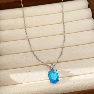 Close-up detail of a minimalist silver necklace with an elegant oval blue zircon pendant.