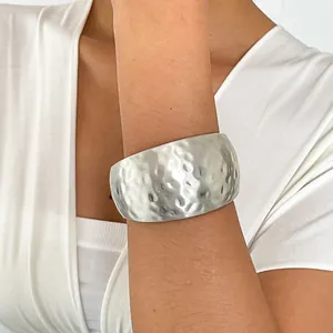 Detailed view of hammered metal cuff bracelet with silver-tone textured finish on model's arm.