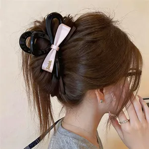 Pince à cheveux élégante en acrylique noir avec nœud en soie rose porté sur chignon.