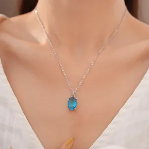 Detailed close-up of an elegant oval blue zircon necklace worn by a model in white clothing