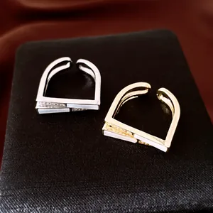 Détail macro de bagues ouvertes carrées géométriques avec zircons et accents de nacre.