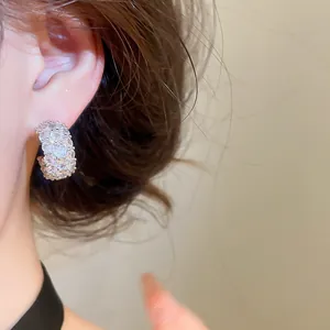 Close-up detail of sparkling zircon C-shaped hoop earrings worn on a model's ear