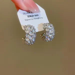 Macro detail of C-shaped earrings with sparkling cubic zirconia on a display card.