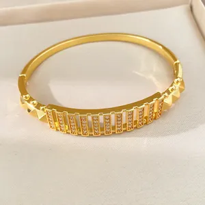 Nahaufnahme eines vergoldeten Armreifs mit Zirkonia-Pflaster und geometrischen Nieten.