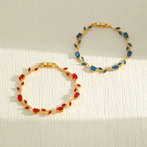 Detailansicht von 18K vergoldeten Blattarmbändern mit roten und blauen Kristallen.
