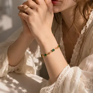 Nahaufnahme eines eleganten Goldblatt Armbands mit grünen und rosa Edelsteinen