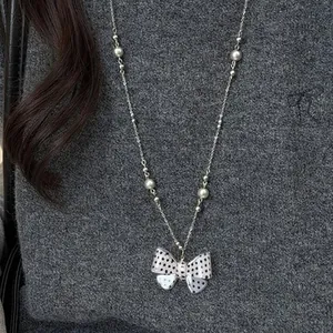 Elegante Perlenkette im koreanischen Stil mit gepunktetem Schleifenanhänger auf grauem Pulli