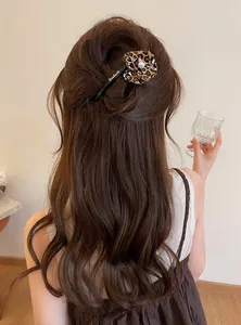 Detailed view of an elegant leopard print flower hair clip worn on wavy brown hair