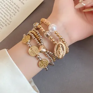Close-up of four-piece beaded bracelet set with heart and religious coin pendants on wrist.