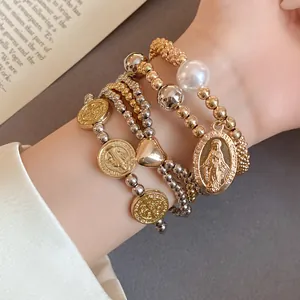 Close-up detail of layered elastic beaded bracelets featuring heart and coin pendants with a pearl