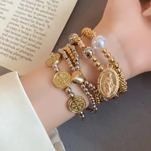 Close-up of 4-piece beaded bracelet set featuring heart and religious coin charms on wrist