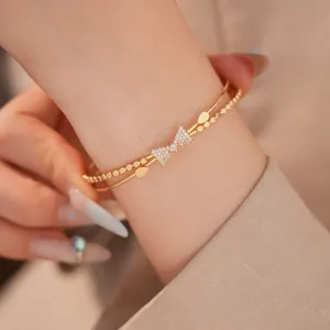 Nahaufnahme eines doppelschichtigen goldenen Schleifen-Armreifs mit Zirkonia am Handgelenk.