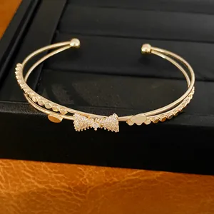 Detailansicht eines doppellagigen goldenen Armreifs mit funkelndem Zirkonia-Schleifen-Design.