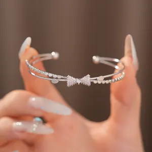 Nahaufnahme eines eleganten silbernen Doppelarmreifs mit einer funkelnden Zirkon-Schleife.