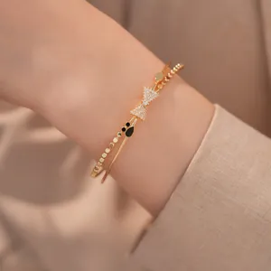 Nahaufnahme eines eleganten Goldarmreifs mit Zirkon-Schleife und Perlenarmband am Handgelenk.