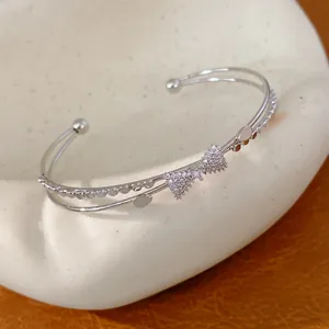 Elegante Nahaufnahme eines zweilagigen Silberarmreifs mit funkelndem Zirkon-Schleifen-Detail.