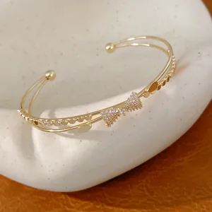 Detailansicht eines zweilagigen goldenen Armreifs mit funkelnder Zirkonia-Schleife