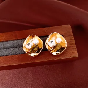 Détail de boucles d'oreilles en plaqué or 18k avec perle, zircon et oeil de tigre.