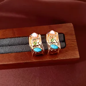 Gros plan de boucles d'oreilles vintage dorées avec perles, turquoise et zircons verts.