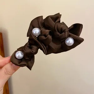 Nahaufnahme einer braunen Satin-Haarspange mit drei eleganten großen weißen Perlen.