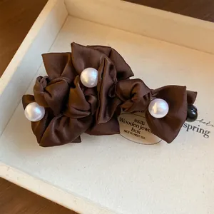 Nahaufnahme einer braunen Stoffschleife Haarklammer mit eleganten weißen Perlen.