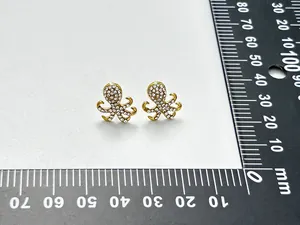 Nahaufnahme von Oktopus-Ohrsteckern mit Kristallen und Goldlegierung mit Lineal