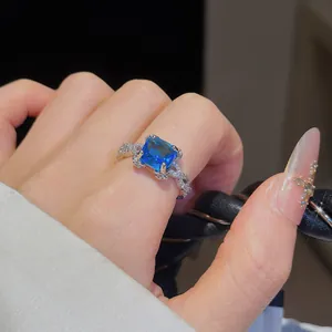 Bague en argent exquise avec zircon bleu carré portée sur une main aux ongles décorés