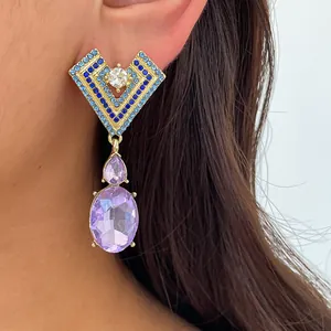 Gros plan de boucles d'oreilles géométriques avec cristaux violets et strass bleus