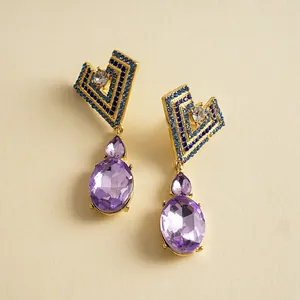 Vue détaillée de boucles d'oreilles dorées géométriques avec cristaux bleus et violets.