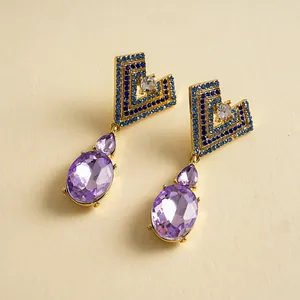 Gros plan de boucles d'oreilles cœur géométriques dorées avec cristaux violets et pierres bleues
