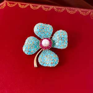 Elegant flower brooch with turquoise stones and central pearl on red background