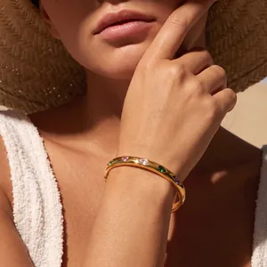 Dettaglio di bracciale in acciaio dorato con zirconi colorati a forma di cuore e goccia.