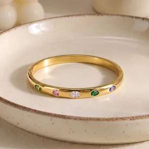 Primo piano di un bracciale in acciaio dorato con gemme colorate a cuore e a goccia.