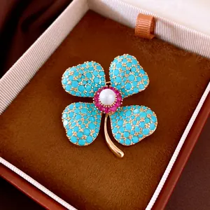 Detailaufnahme einer Vintage-Blumenbrosche mit türkisfarbenen Steinen und zentraler Perle