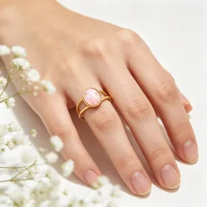 Detailed view of a vintage oval pink cat's eye stone ring worn on a hand with flowers