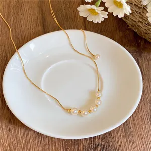 Detailed macro view of gold chain necklace with round white pearls on a white plate.