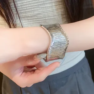Detailed close-up of a wide metallic textured silver open cuff bracelet on wrist.