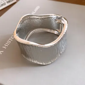 Macro view of a textured silver metal wide cuff bracelet with elegant wavy surface design