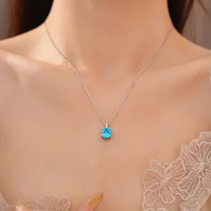 Close-up van een zilverkleurige ketting met een helderblauwe zirkoon hanger om de nek van een vrouw.